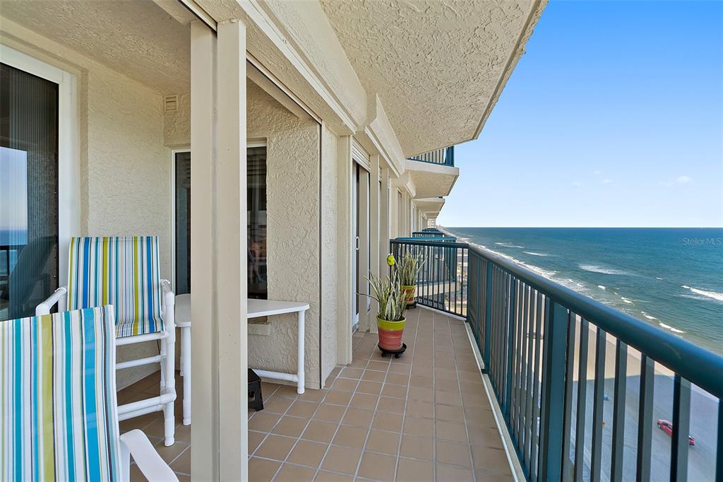 A tiled balcony overlooks the ocean with striped chairs, potted plants, and a metal railing — 3425 S ATLANTIC AVENUE UNIT 1206, DAYTONA BEACH SHORES, FL