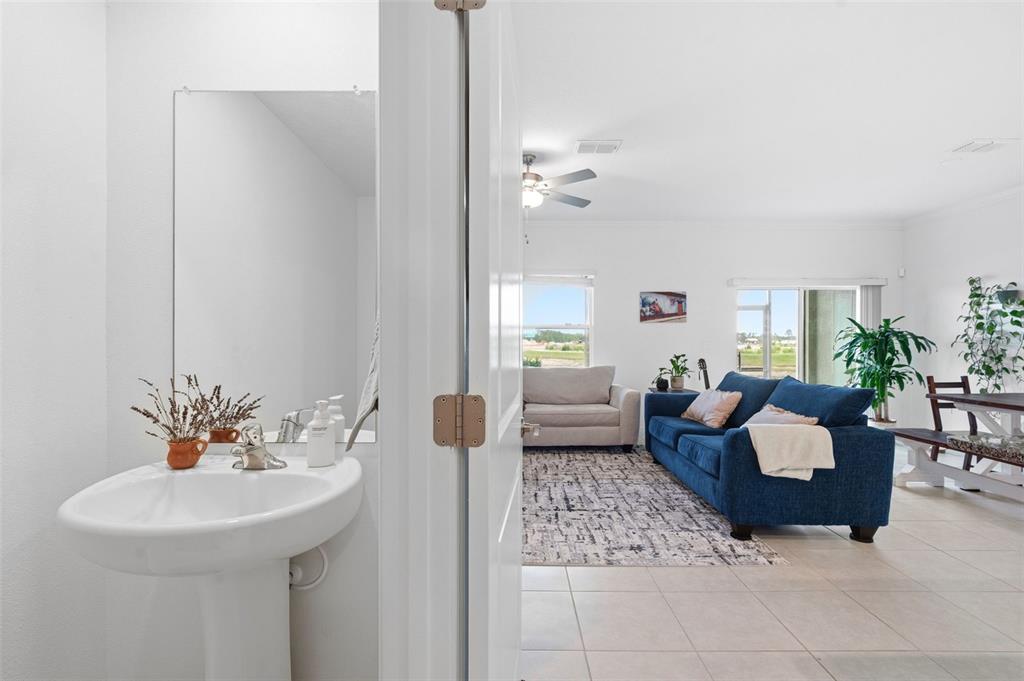 A pedestal sink in a small bathroom looks out toward a living room with furniture — 9124 GALLANTREE PLACE, LAND O LAKES, FL
