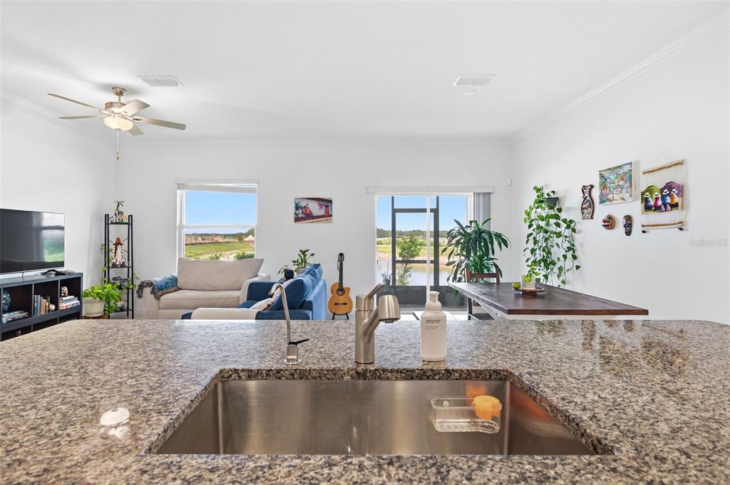 A kitchen island with a granite countertop and stainless steel sink overlooks an open-concept living area — 9124 GALLANTREE PLACE, LAND O LAKES, FL
