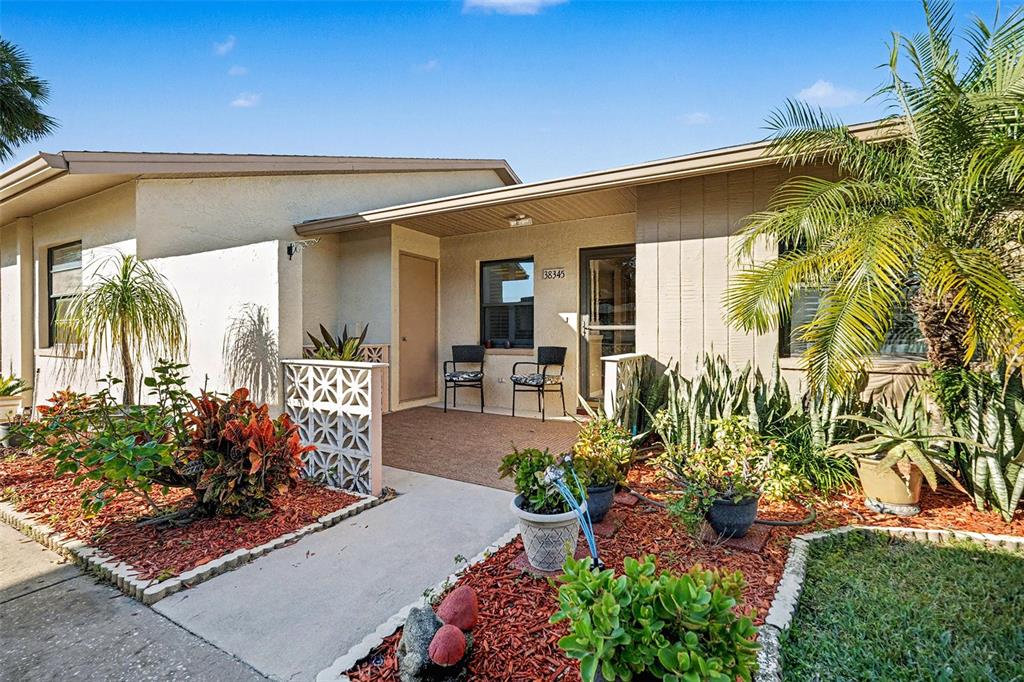 A single-story house exterior features a covered entryway, a small patio, and landscaped garden beds — 38345 COTTONWOOD PLACE UNIT 38345, ZEPHYRHILLS, FL