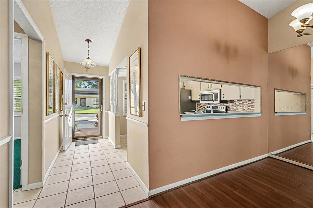 An entryway with tile flooring leads to a front door, with a kitchen pass-through window — 38345 COTTONWOOD PLACE UNIT 38345, ZEPHYRHILLS, FL