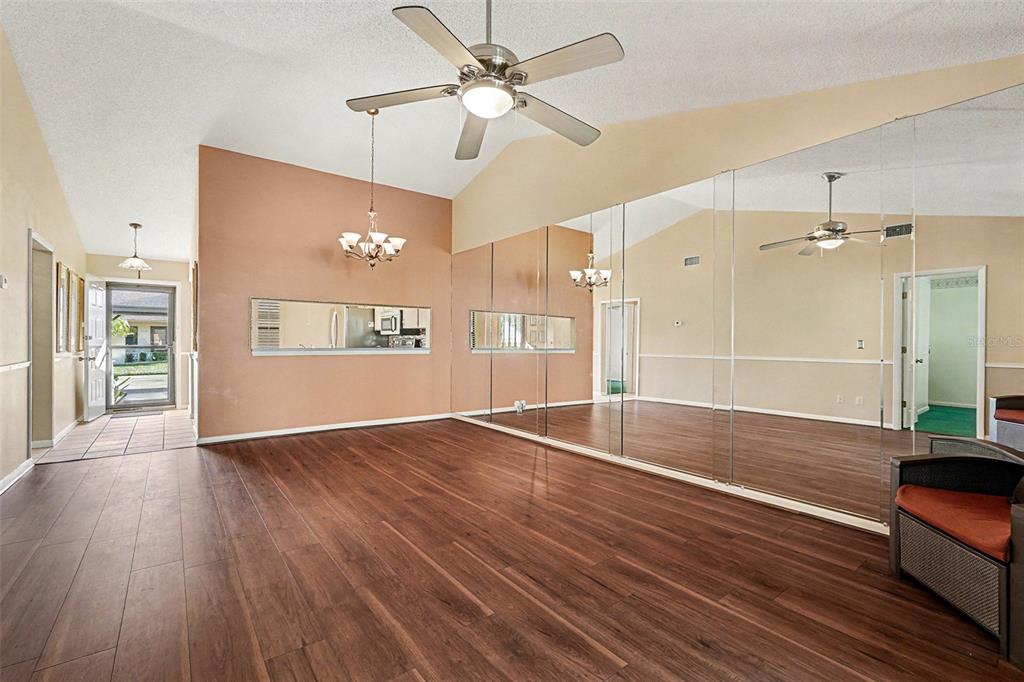 A room with wood-look flooring, a vaulted ceiling, a ceiling fan, and mirrored walls — 38345 COTTONWOOD PLACE UNIT 38345, ZEPHYRHILLS, FL