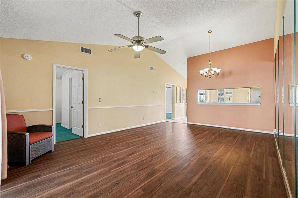 A living room features wood-look flooring, a vaulted ceiling with a fan, and mirrored walls — 38345 COTTONWOOD PLACE UNIT 38345, ZEPHYRHILLS, FL