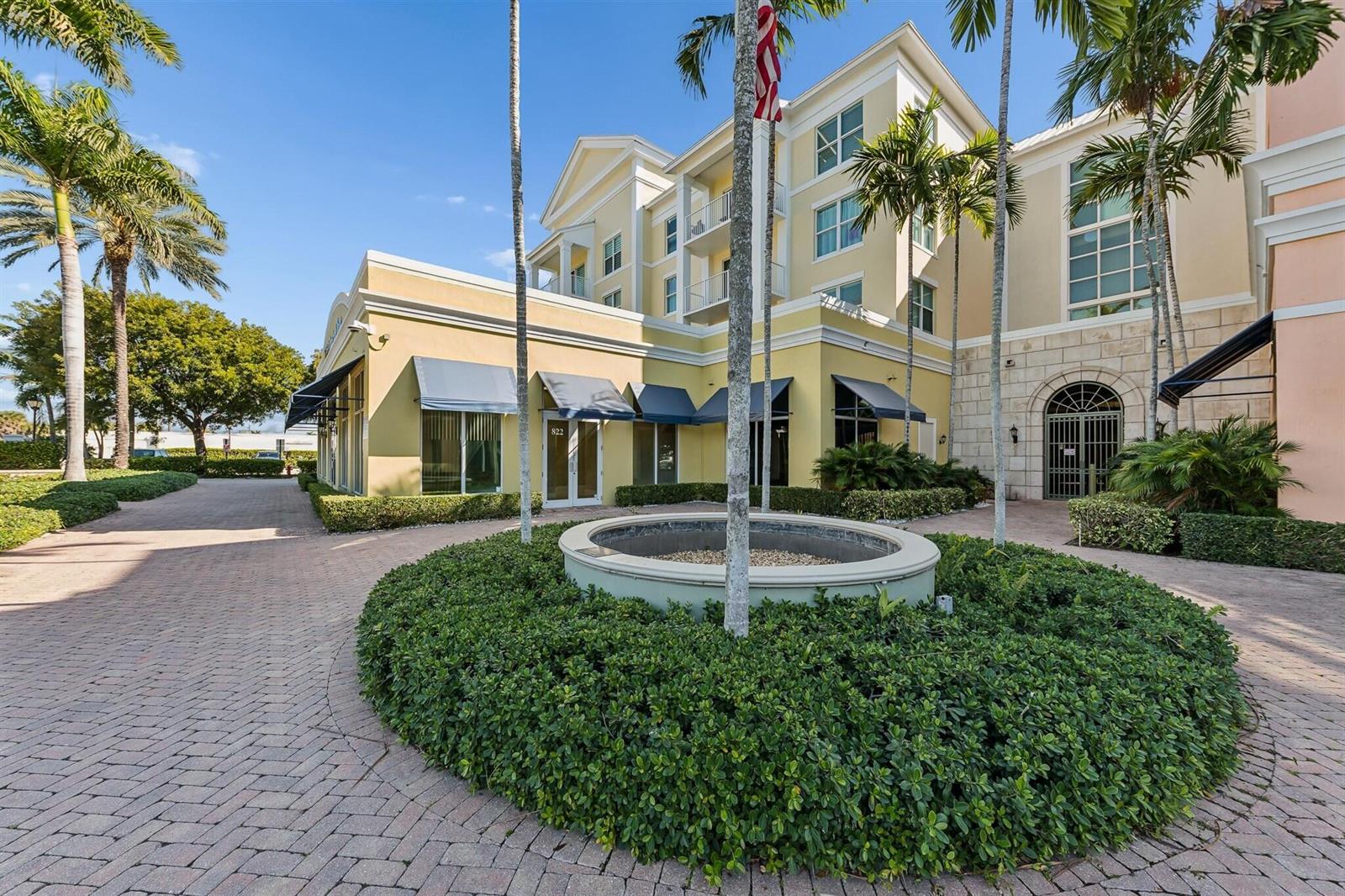 A multi-story yellow building features a circular fountain and palm trees in the courtyard — 826 N Dixie Highway # 15, Lantana FL 33462, LANTANA, FL