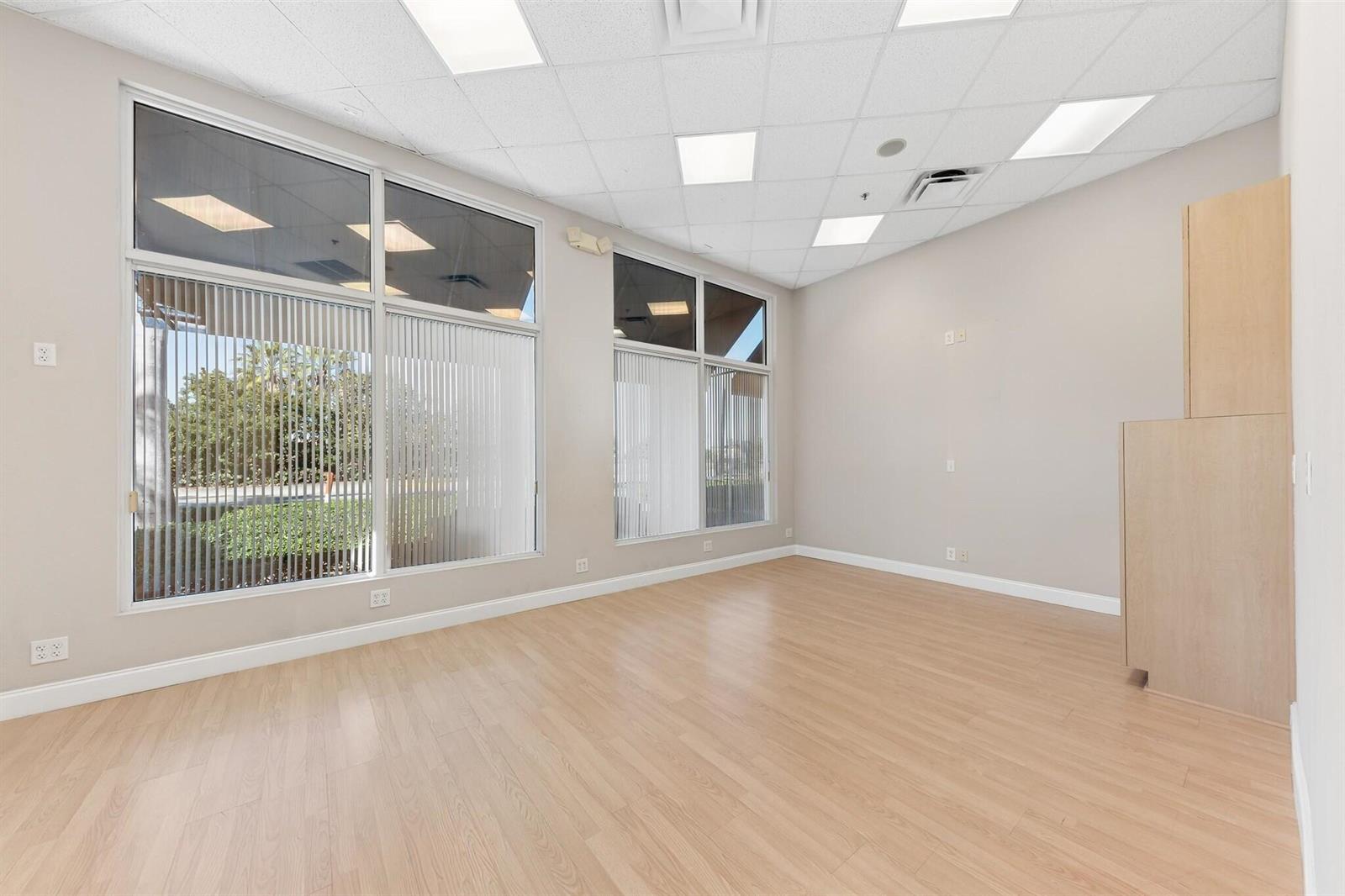 An empty office space with light wood flooring, large windows, and a built-in cabinet — 826 N Dixie Highway # 15, Lantana FL 33462, LANTANA, FL