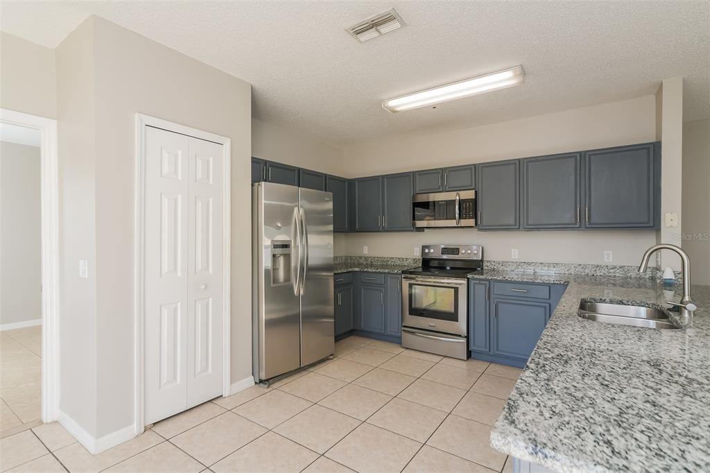 A kitchen features blue cabinets, stainless steel appliances, granite countertops, and light-colored floor tiles — 4417 CANOPY COURT, KISSIMMEE, FL