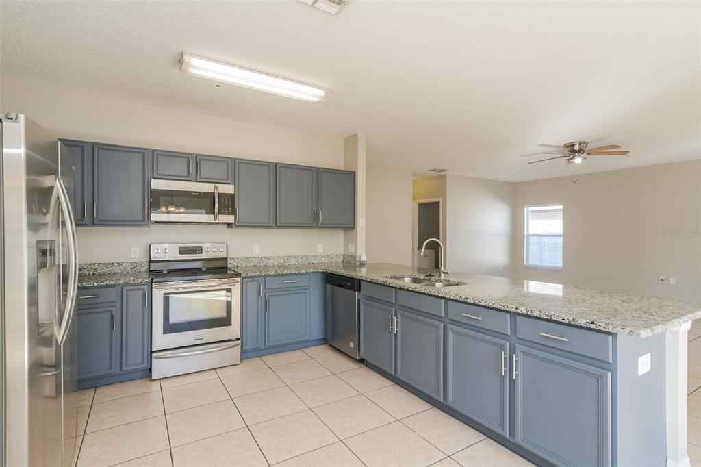 A kitchen with blue cabinets, granite countertops, stainless steel appliances, and light-colored tile flooring — 4417 CANOPY COURT, KISSIMMEE, FL
