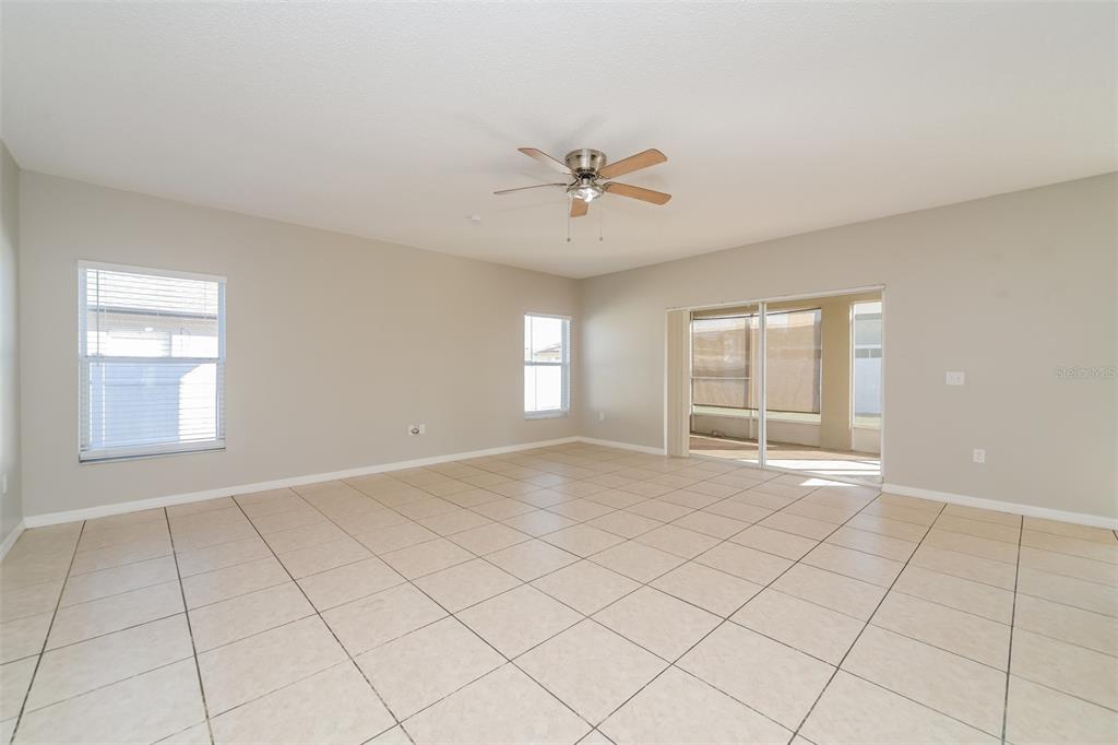 An empty living room features beige tile flooring, a ceiling fan, and sliding glass doors — 4417 CANOPY COURT, KISSIMMEE, FL