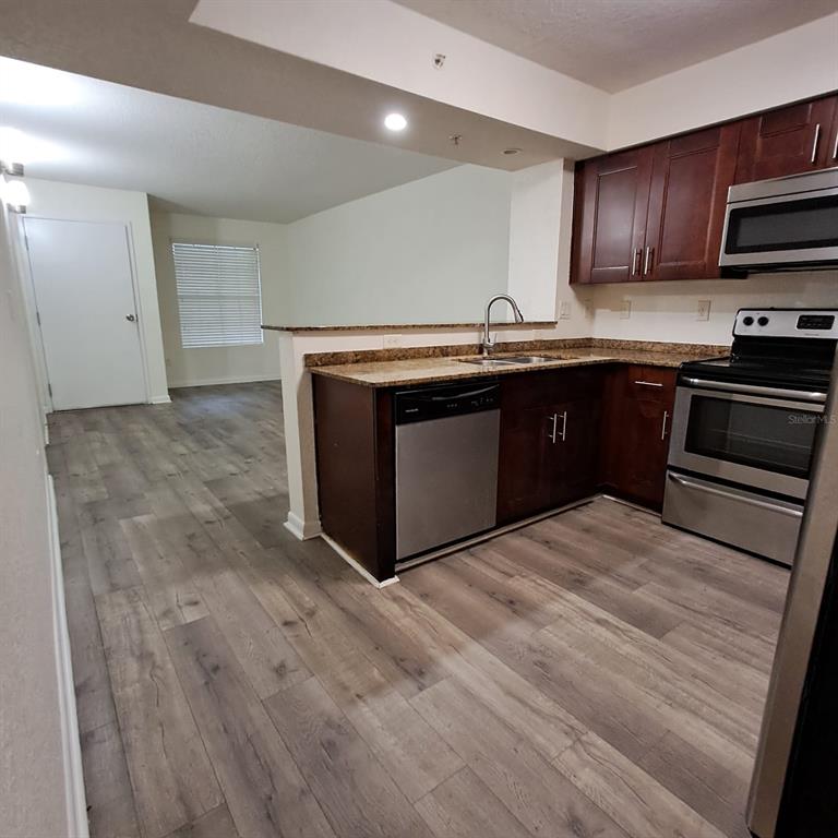 A kitchen with dark wood cabinets, stainless steel appliances, and wood-look flooring — 2323 MCCOY ROAD UNIT 711, ORLANDO, FL