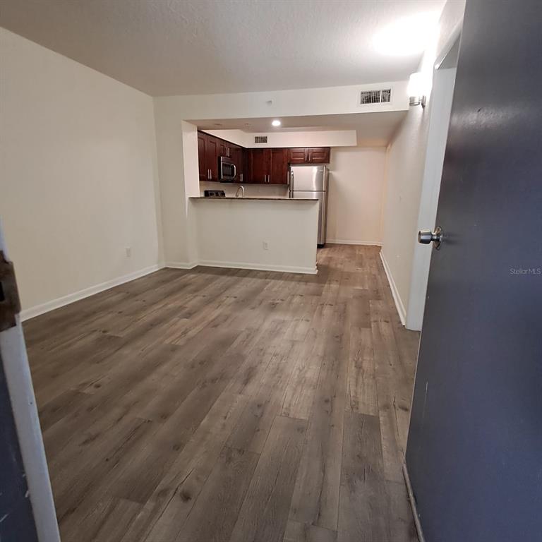 A view from a doorway into an open-concept living area with wood-look flooring and kitchen — 2323 MCCOY ROAD UNIT 711, ORLANDO, FL