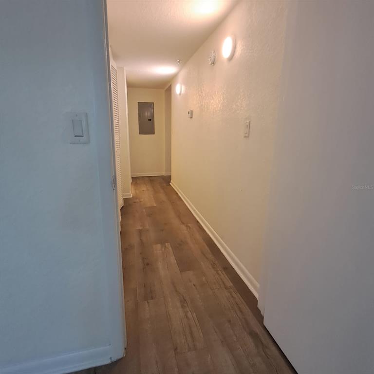 A hallway with wood-look flooring, white walls, and a visible electrical panel at the end — 2323 MCCOY ROAD UNIT 711, ORLANDO, FL
