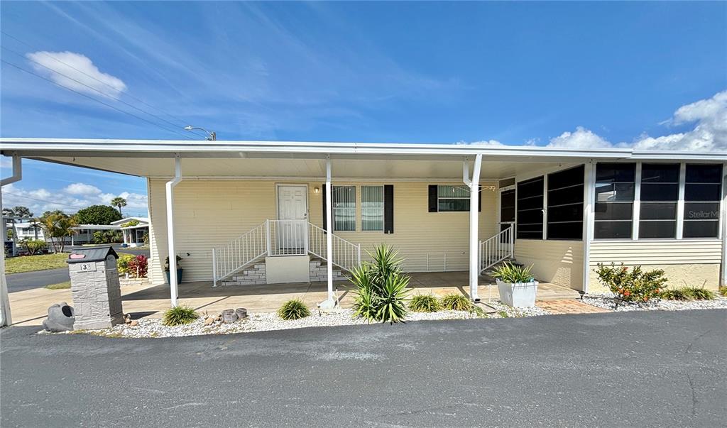 A light yellow mobile home features a covered carport, white railings, and a paved driveway — 136 AMERICANA COURT NE UNIT 230, ST PETERSBURG, FL