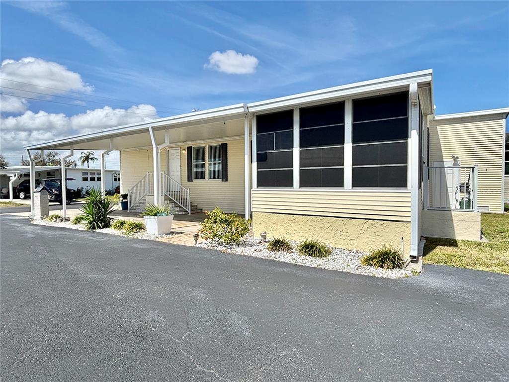 A light yellow manufactured home features a large carport, a screened porch, and gravel landscaping — 136 AMERICANA COURT NE UNIT 230, ST PETERSBURG, FL
