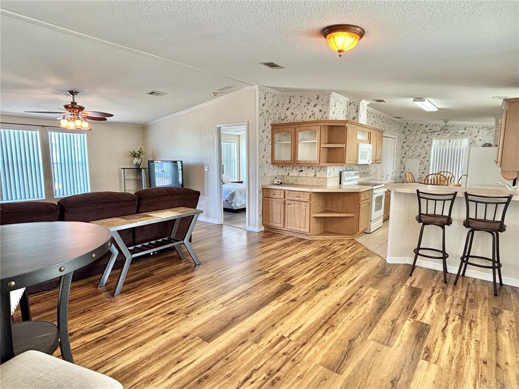An open-concept living room and kitchen featuring wood-look flooring and light oak cabinetry — 136 AMERICANA COURT NE UNIT 230, ST PETERSBURG, FL