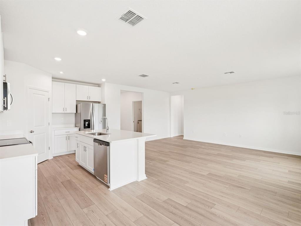 A modern kitchen with white cabinets and a center island opens to a living area — 10404 ABUNDANCE GROVE WAY, PARRISH, FL