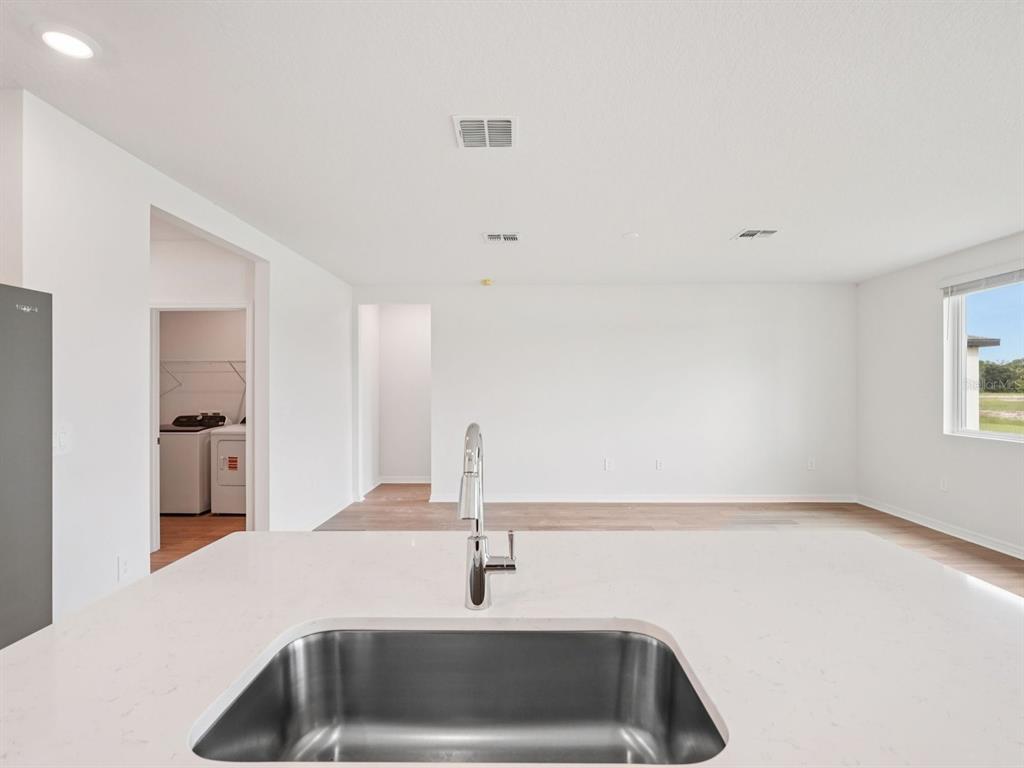 A kitchen island with a stainless steel sink overlooks an open living area and laundry room — 10404 ABUNDANCE GROVE WAY, PARRISH, FL