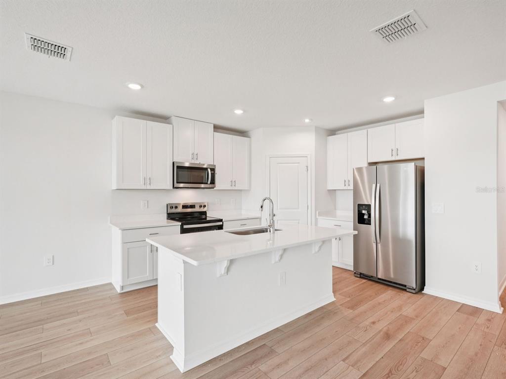 A modern kitchen features white cabinets, stainless steel appliances, a center island, and wood flooring — 10404 ABUNDANCE GROVE WAY, PARRISH, FL