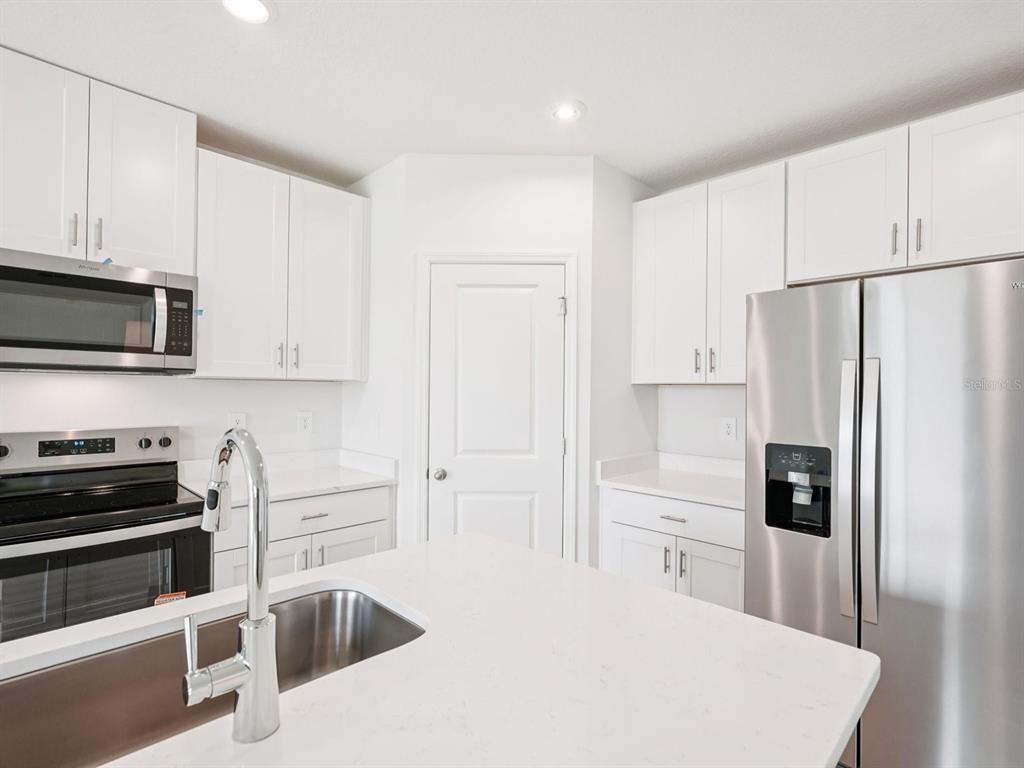 A modern kitchen features white cabinets, stainless steel appliances, and a white quartz island countertop — 10404 ABUNDANCE GROVE WAY, PARRISH, FL