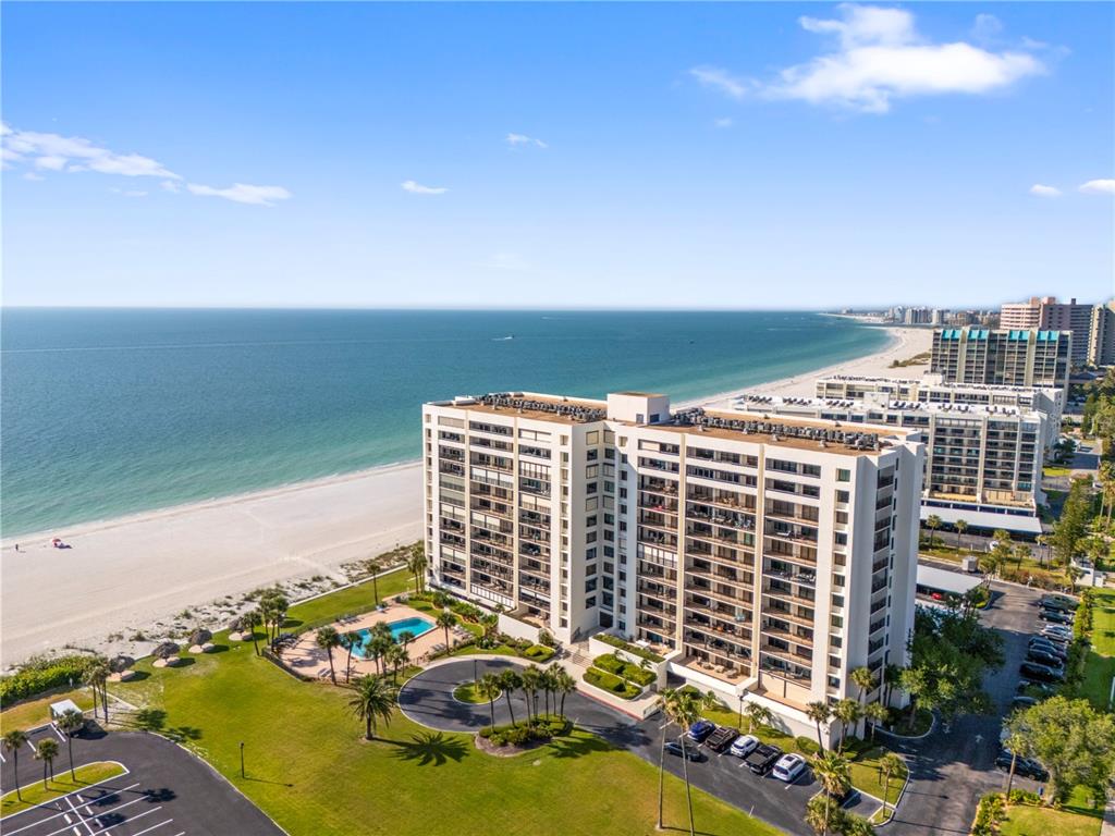 An aerial view shows a large beachfront condominium building with a pool and parking lot — 1460 GULF BOULEVARD UNIT 412, CLEARWATER BEACH, FL