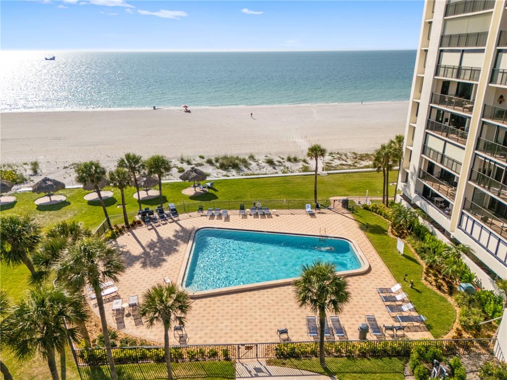 An aerial view of a swimming pool and patio area next to a beachside building — 1460 GULF BOULEVARD UNIT 412, CLEARWATER BEACH, FL