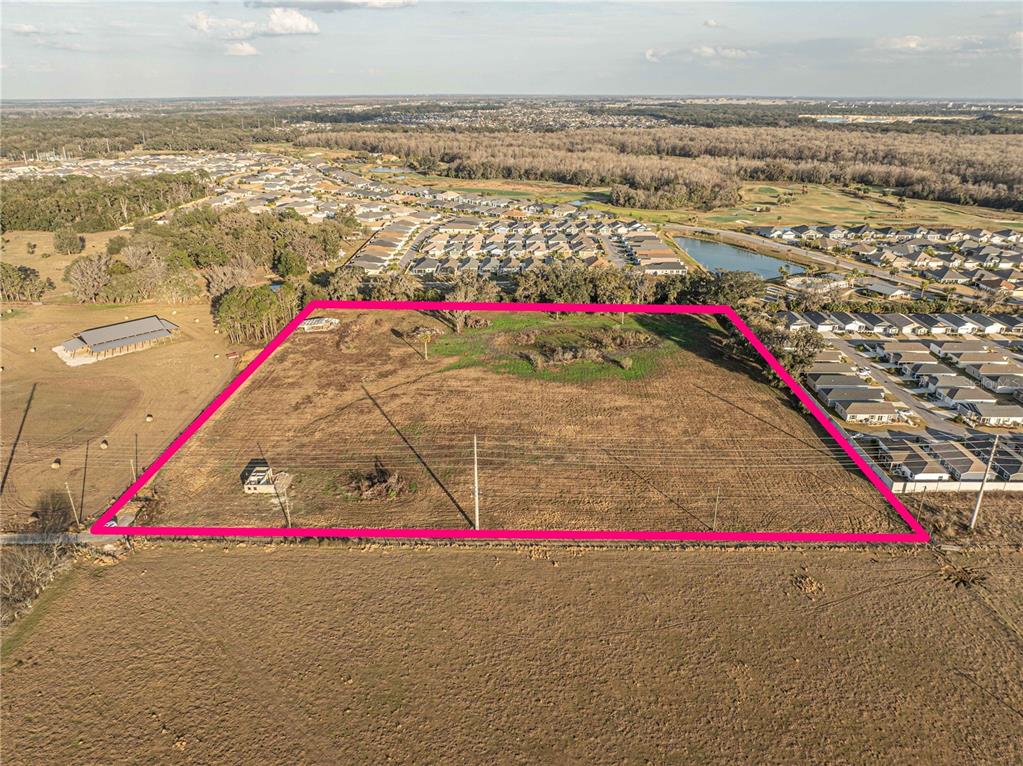 An aerial view shows a large, rectangular vacant lot outlined in pink near a residential neighborhood — 2619 COUNTY ROAD 523, WILDWOOD, FL