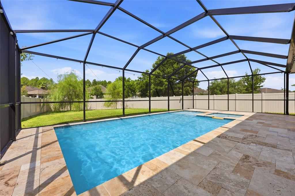 A rectangular swimming pool with a spa sits inside a screened-in patio with stone pavers — 2408 LAS CALINAS BOULEVARD, ST AUGUSTINE, FL