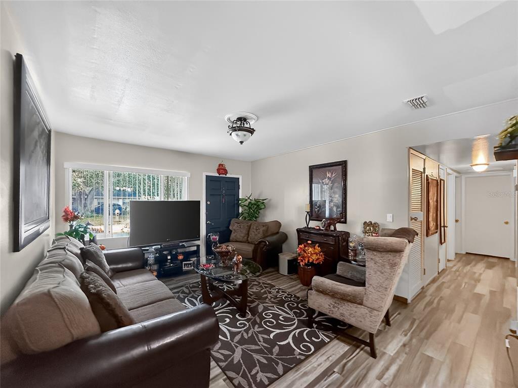A living room features a brown sofa, an armchair, a television, and light wood flooring — 8009 CORNWALL LANE, TAMPA, FL