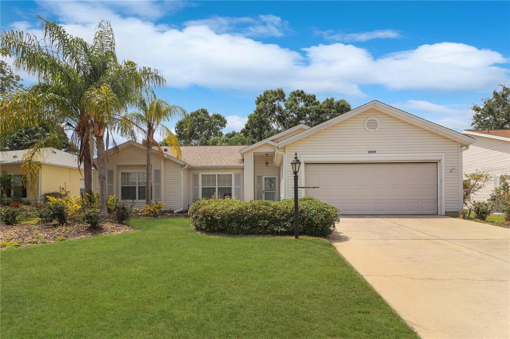 A single-story house with beige siding, a two-car garage, and a palm tree in front — 25339 CRESTWATER DRIVE, LEESBURG, FL