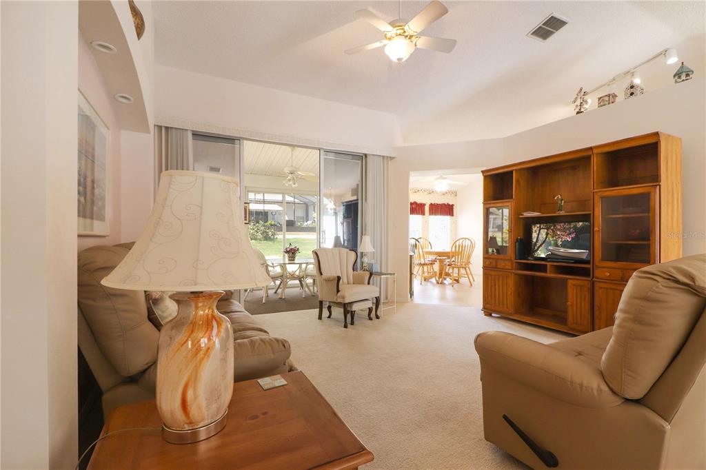 A living room features beige carpet, a wooden entertainment center, and a sliding glass door — 25339 CRESTWATER DRIVE, LEESBURG, FL