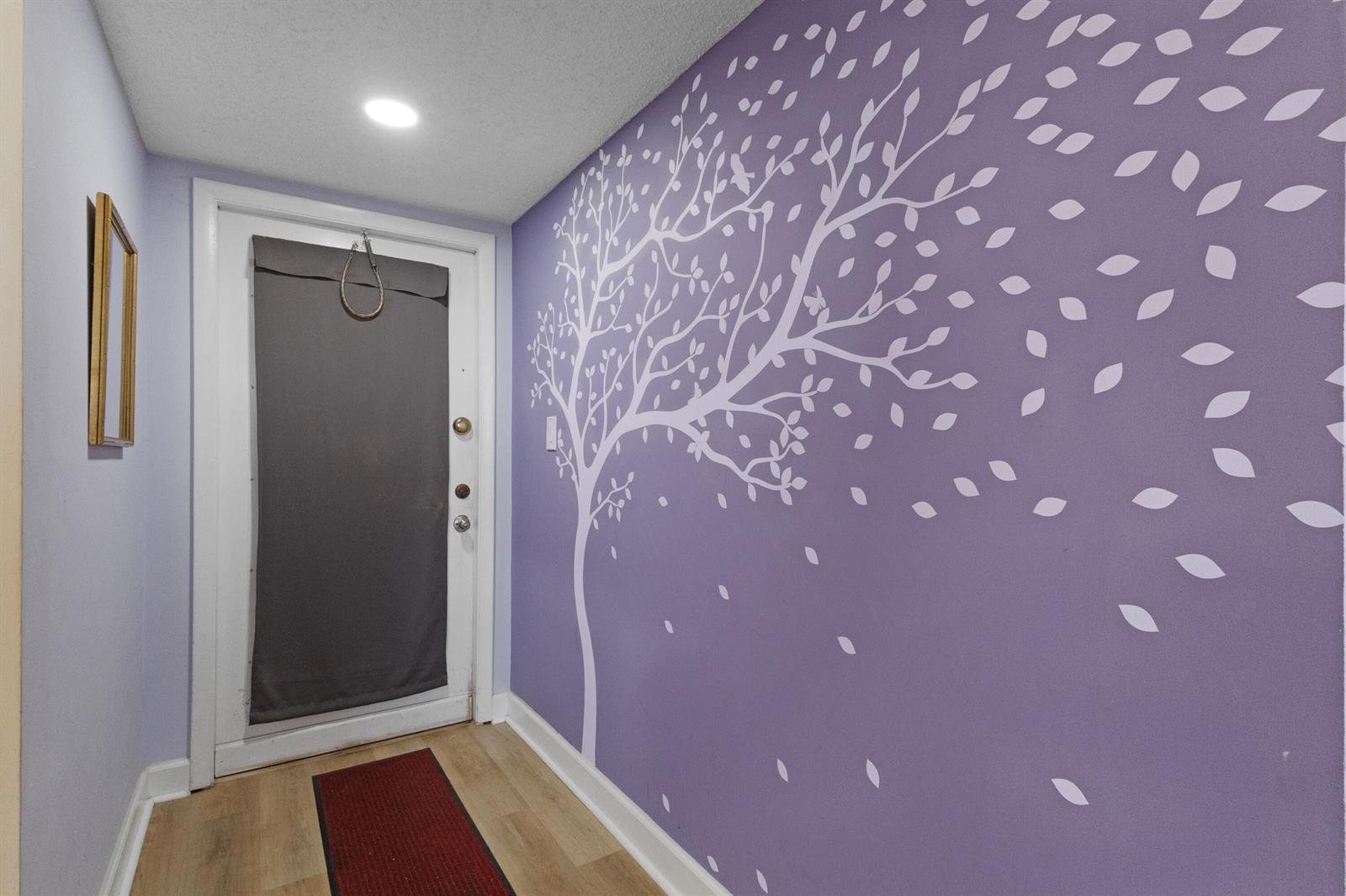 A hallway features light wood flooring, a purple wall with a white tree decal, and a door — 6870 Royal Palm Boulevard # 202m, Margate FL 33063, MARGATE, FL