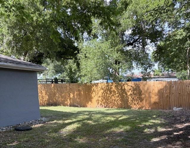 A view of a backyard featuring a wooden privacy fence, green grass, and mature trees — 5719 14TH STREET E, BRADENTON, FL