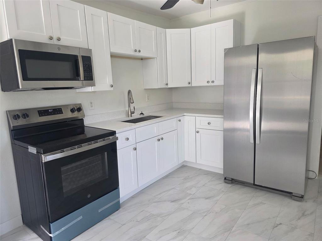 A kitchen features white cabinets, stainless steel appliances, a sink, and light-colored tile flooring — 5719 14TH STREET E, BRADENTON, FL