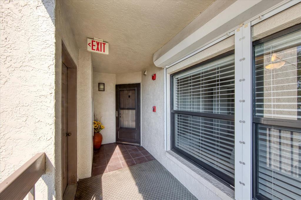 An exterior entryway features a tiled floor, a brown door, and an illuminated exit sign — 1324 PASADENA AVENUE S UNIT 201, SOUTH PASADENA, FL