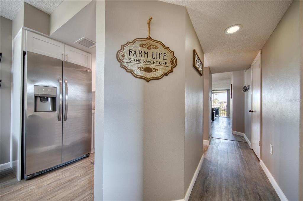 A hallway with wood-look flooring leads past a stainless steel refrigerator to a balcony — 1324 PASADENA AVENUE S UNIT 201, SOUTH PASADENA, FL