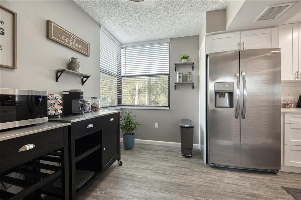 A kitchen area features a stainless steel refrigerator, black cabinetry, and a corner window — 1324 PASADENA AVENUE S UNIT 201, SOUTH PASADENA, FL