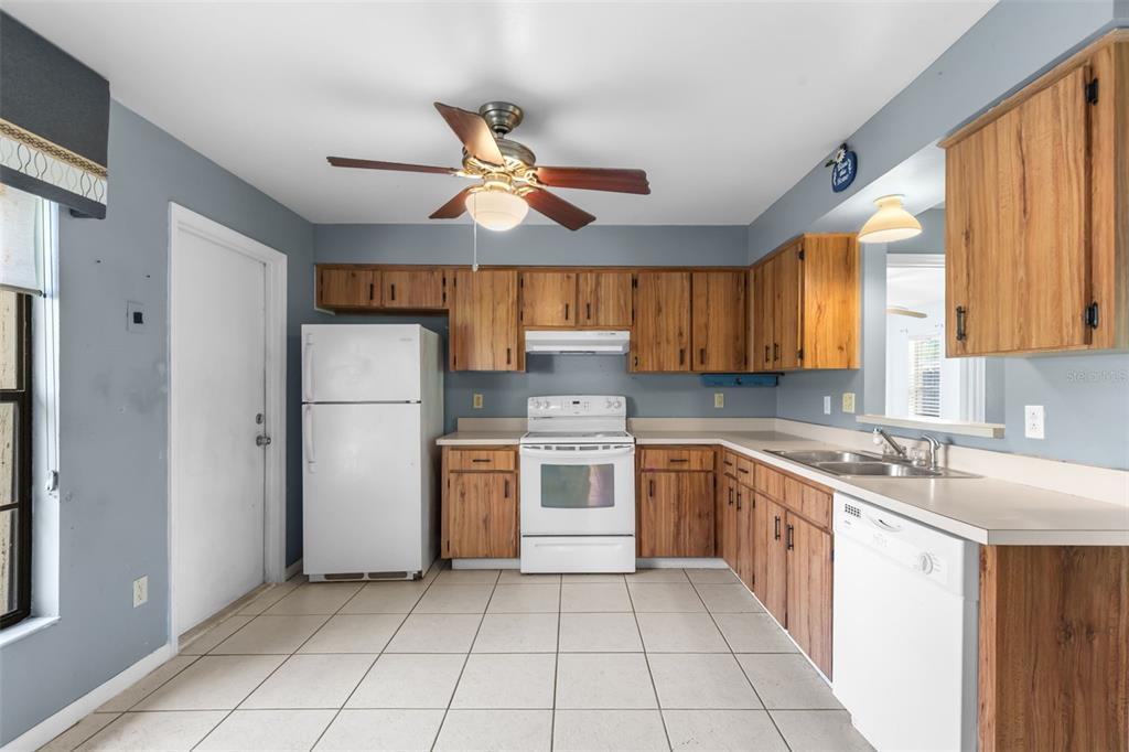 A kitchen with wood cabinets, white appliances, tile flooring, and a ceiling fan — 17635 MEADOWBRIDGE DRIVE, LUTZ, FL