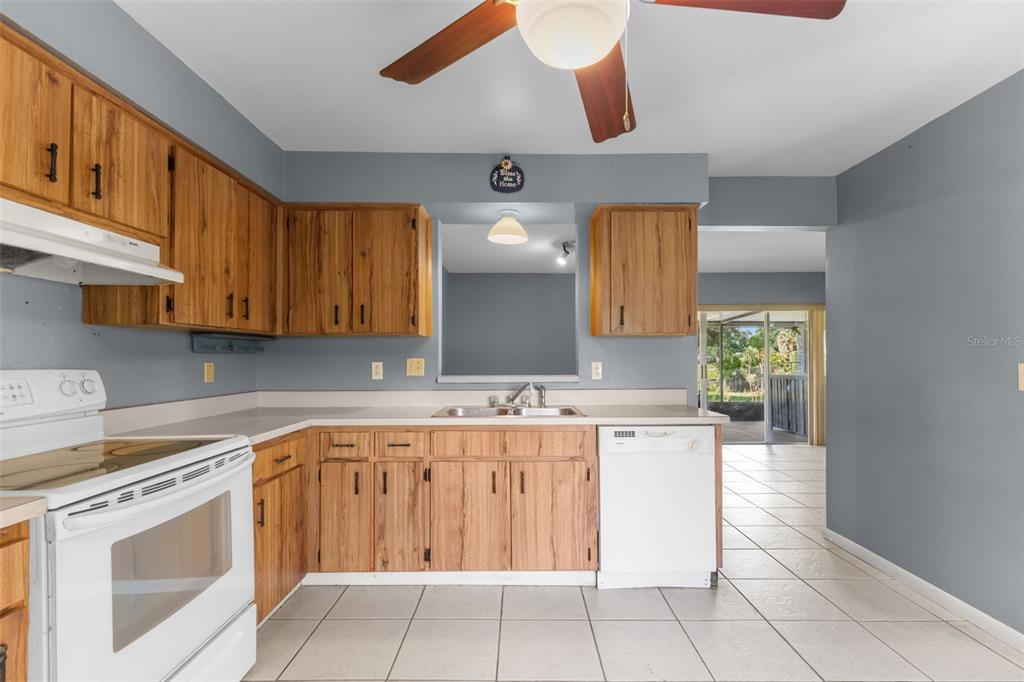 A kitchen features wood cabinets, white appliances, a pass-through window, and light-colored tile flooring — 17635 MEADOWBRIDGE DRIVE, LUTZ, FL