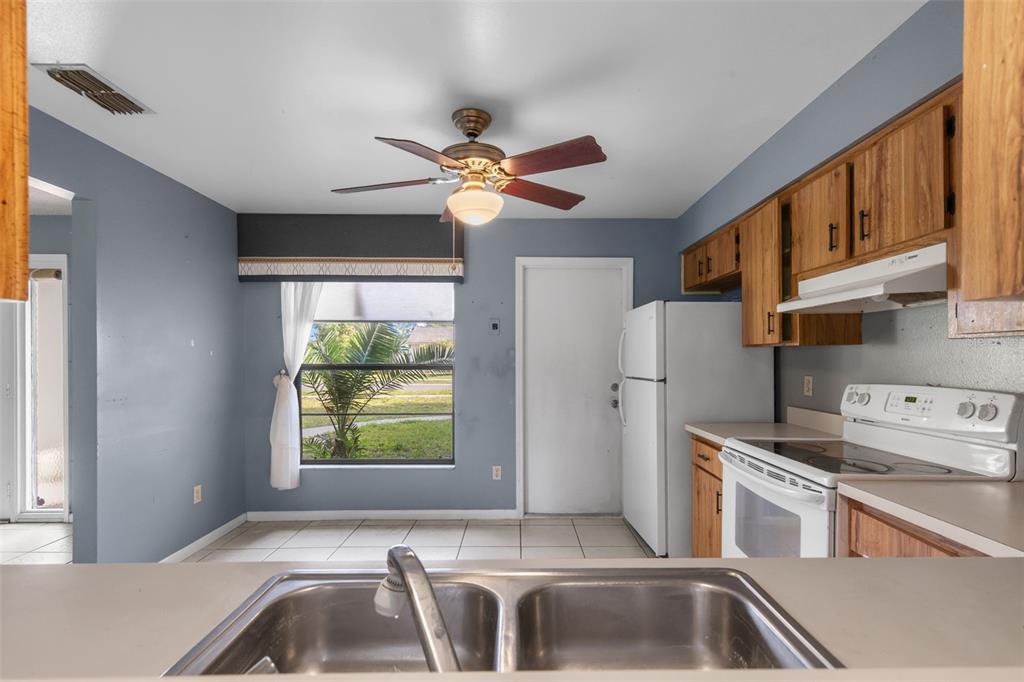 A kitchen with wood cabinets, white appliances, a double sink, and a dining area — 17635 MEADOWBRIDGE DRIVE, LUTZ, FL