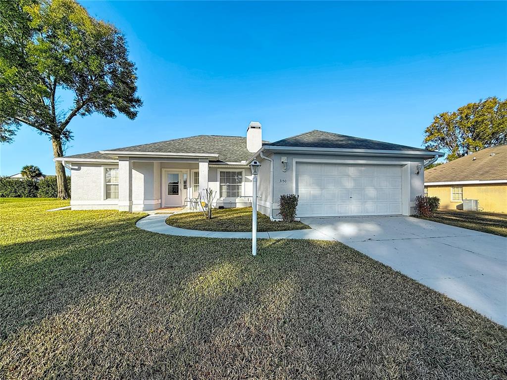 A single-story house with a white stucco exterior, a two-car garage, and a large lawn — 3150 NW 50TH COURT, OCALA, FL