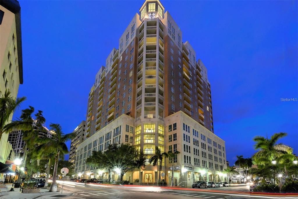 A tall, multi-story residential building with balconies stands at a street corner at dusk — 1350 MAIN STREET UNIT 709, SARASOTA, FL