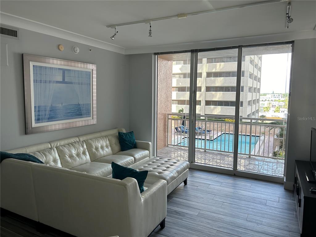 A living room with a white sectional sofa, wood-look tile floors, and a balcony view — 1350 MAIN STREET UNIT 709, SARASOTA, FL
