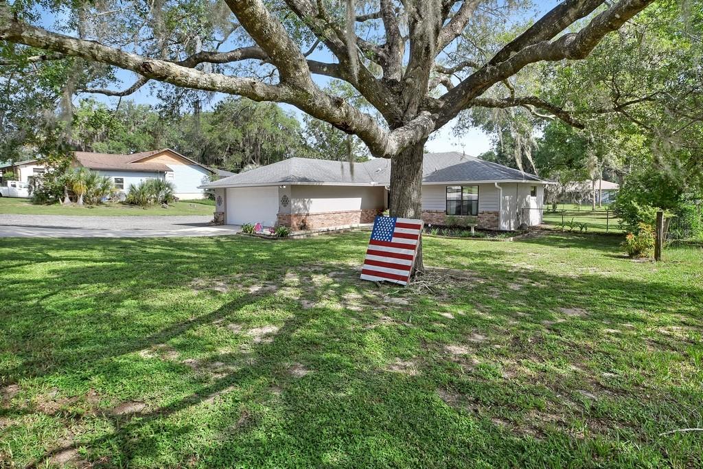 A single-story house with a garage and a wooden American flag sign under a tree — 235 W RETTA STREET, DE LEON SPRINGS, FL