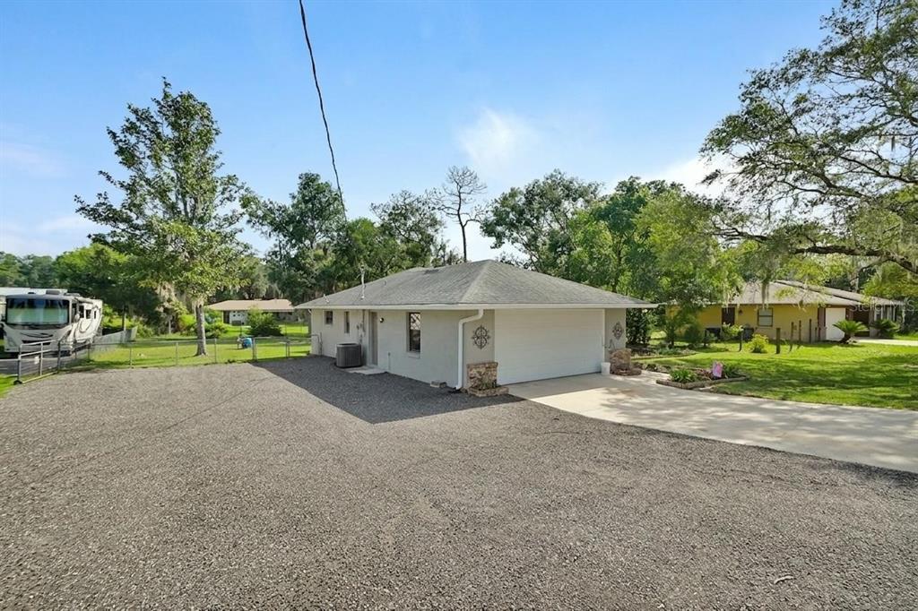 A light-colored house with a gravel driveway, a two-car garage, and surrounding trees — 235 W RETTA STREET, DE LEON SPRINGS, FL