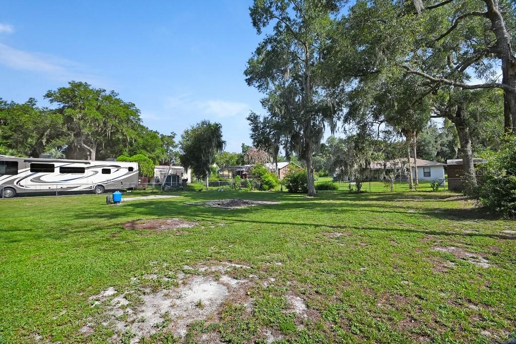 A large, grassy backyard features a parked recreational vehicle and several mature oak trees — 235 W RETTA STREET, DE LEON SPRINGS, FL