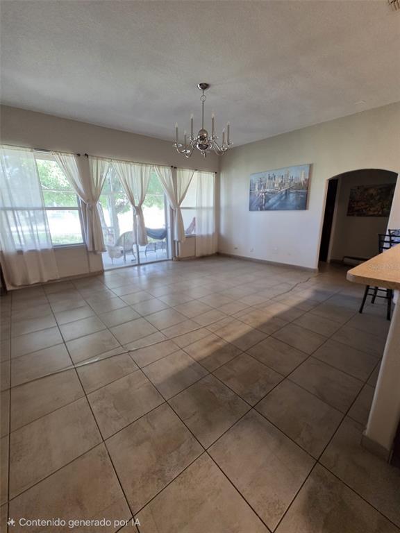 An empty room with light-colored tile flooring, a chandelier, and large windows with curtains — 407 MARTIGUES DRIVE, KISSIMMEE, FL
