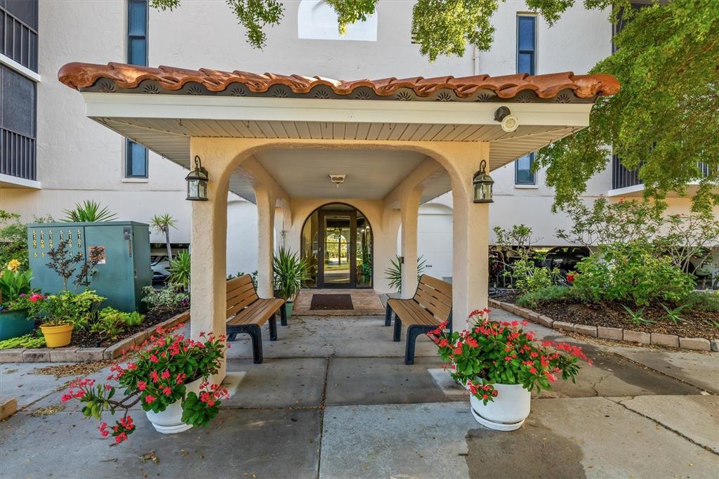 A covered entryway with two wooden benches and potted flowers leads to a glass door — 25188 MARION AVENUE UNIT A108, PUNTA GORDA, FL