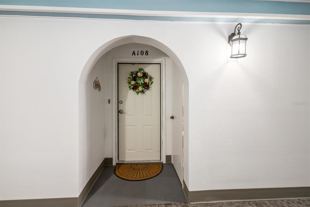 An arched entryway leads to a white door labeled A108 with a floral wreath — 25188 MARION AVENUE UNIT A108, PUNTA GORDA, FL