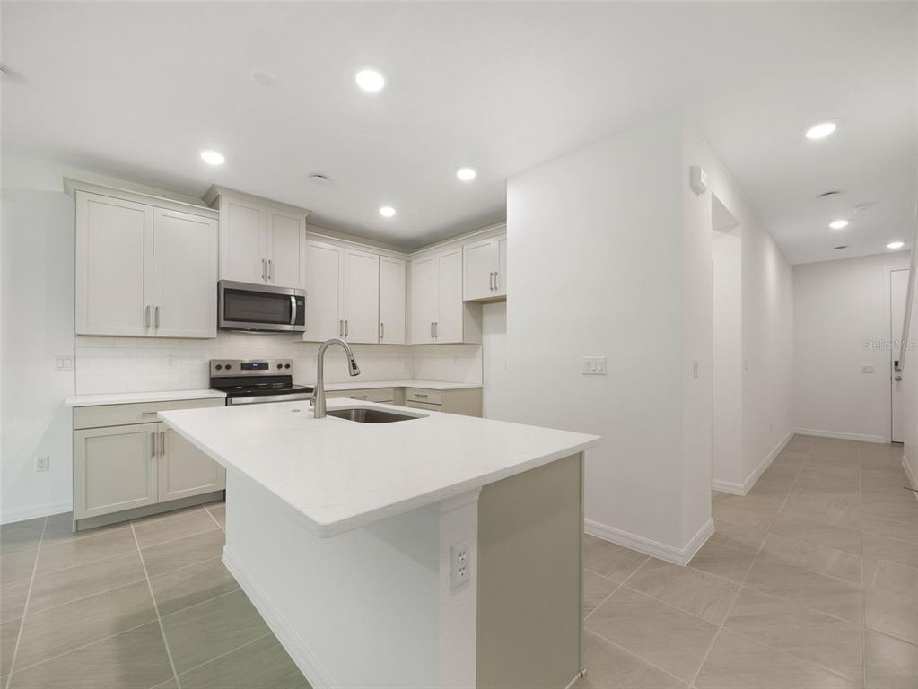A modern kitchen features light-colored cabinetry, a central island with a sink, and tile flooring — 1649 GREENLEAF WOOD COVE, OVIEDO, FL