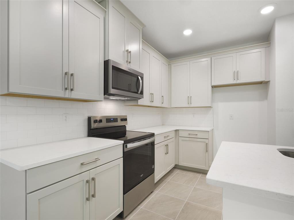 A modern kitchen features light gray cabinets, stainless steel appliances, and white quartz countertops — 1649 GREENLEAF WOOD COVE, OVIEDO, FL