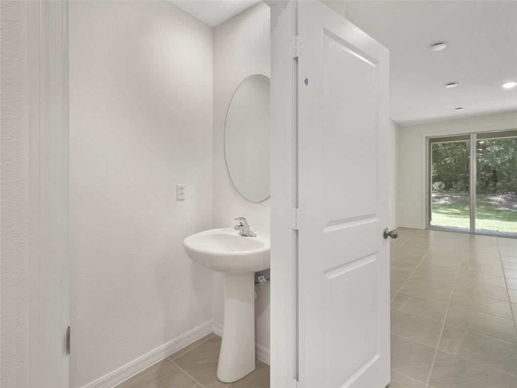 A small bathroom with a pedestal sink and oval mirror opens into a tiled room — 1649 GREENLEAF WOOD COVE, OVIEDO, FL